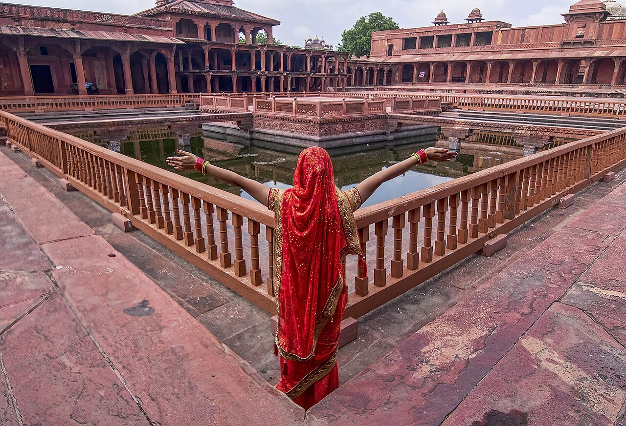 A visitor stands beside the Anup Talao pool and its central platform at Fatehpur Sikri.