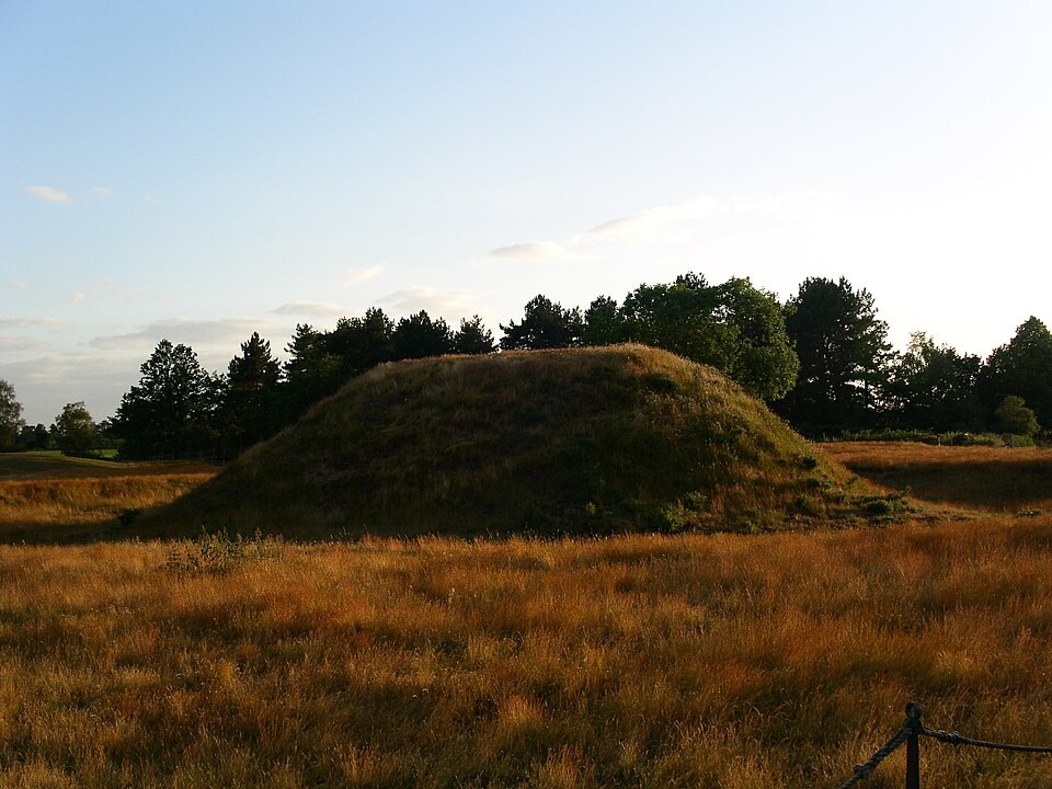 A reconstructed grass-covered burial mound beneath an open sky at Sutton Hoo.