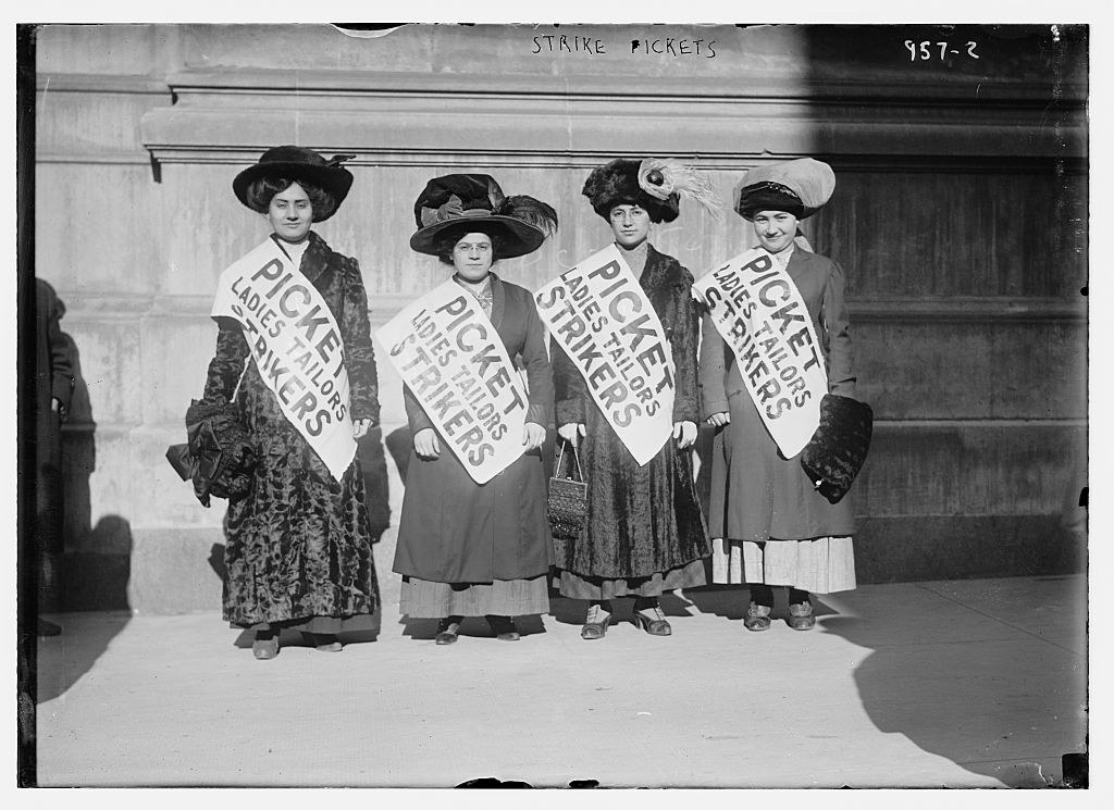 Women wearing hats and picket sashes standing together.