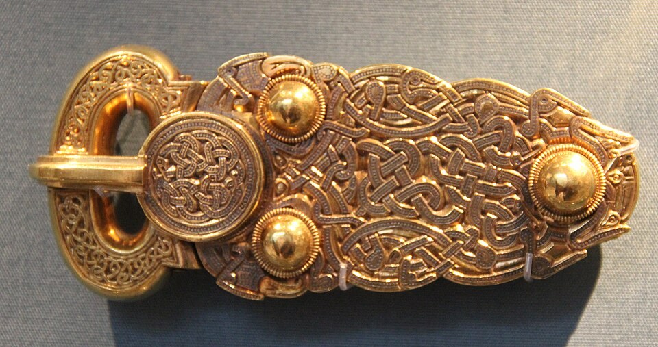 Gold buckle with an oval loop, three rounded bosses and dense interlaced animal ornament.