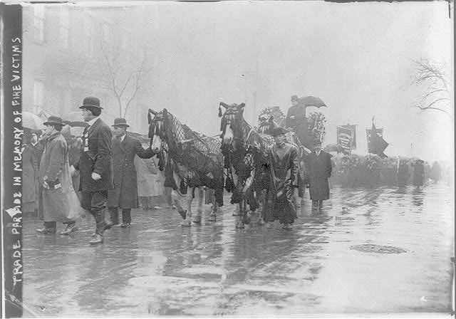 Horse-drawn procession with people and horses draped in black.