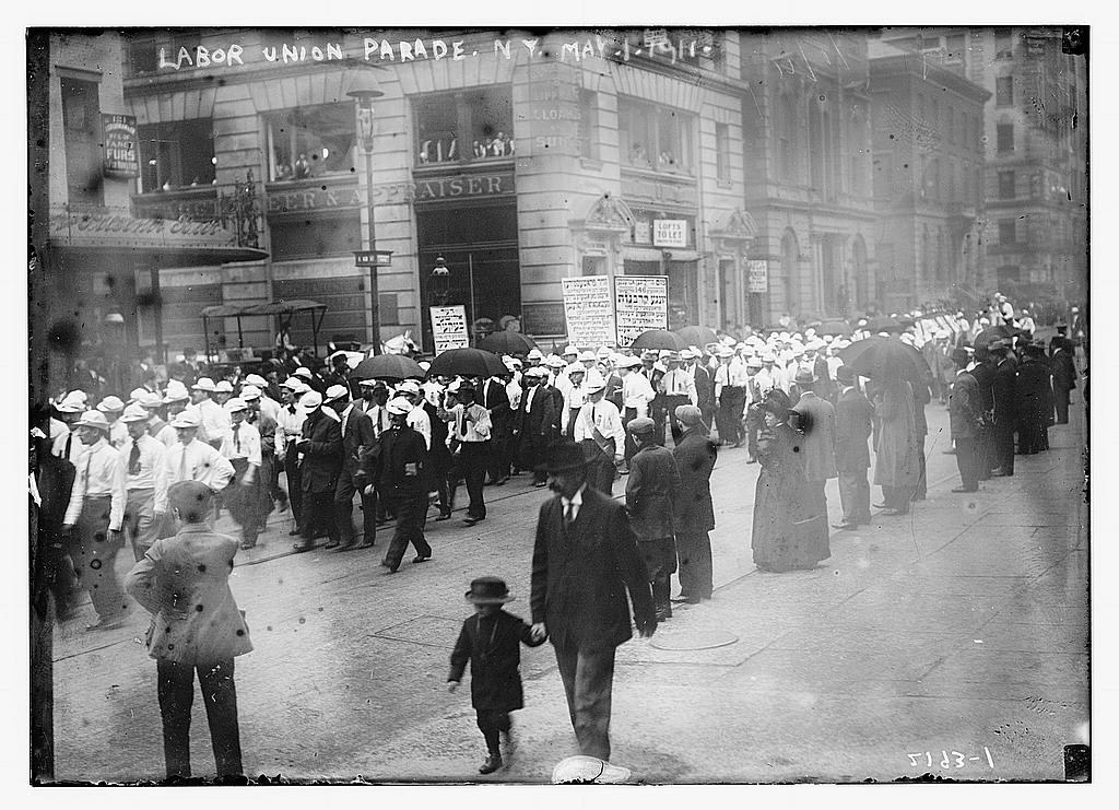 Large labor parade passing a New York street corner with banners.