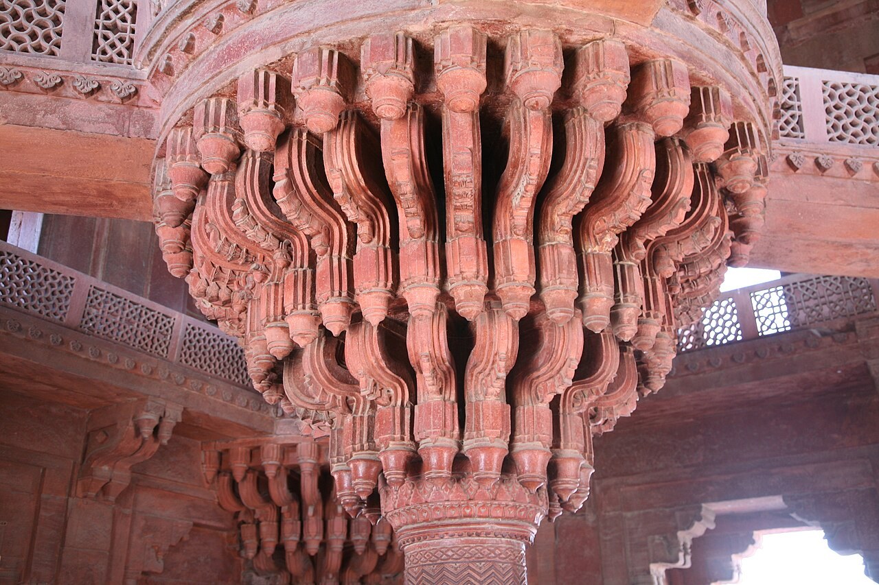 Elaborately carved red-sandstone brackets spreading from a central column inside the Diwan-i-Khas.