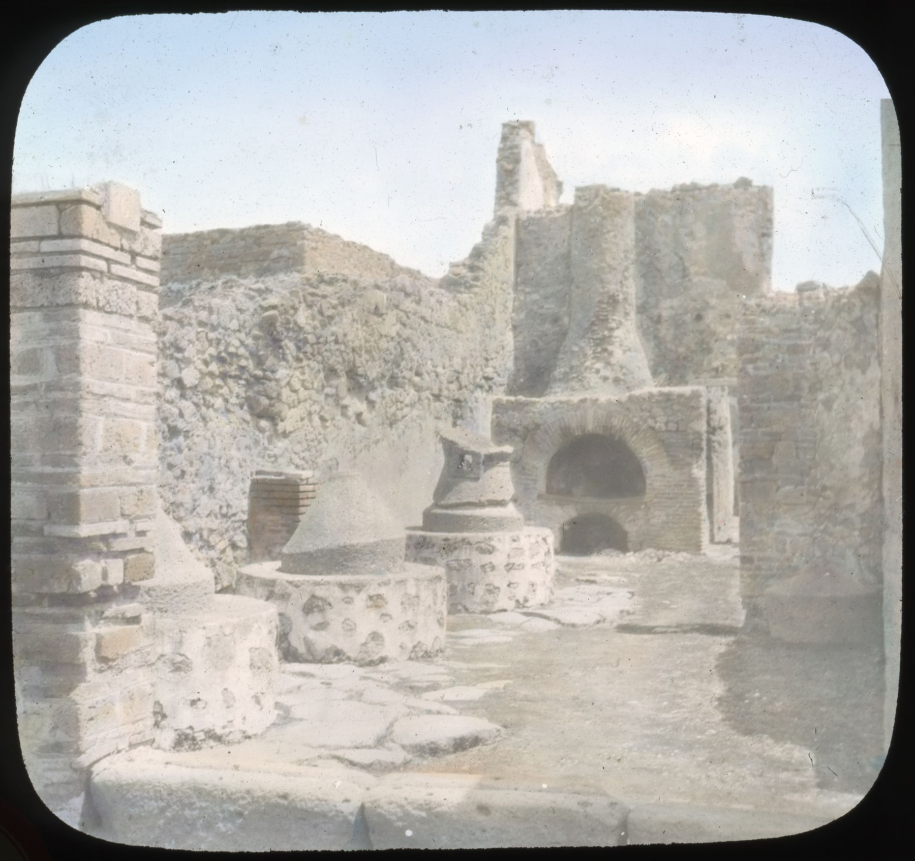Historical lantern-slide photograph of stone mills and an excavated bakery oven.