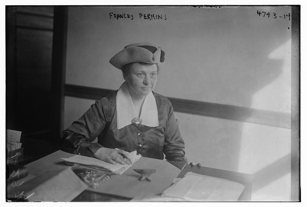 Frances Perkins seated at a table, wearing a hat.