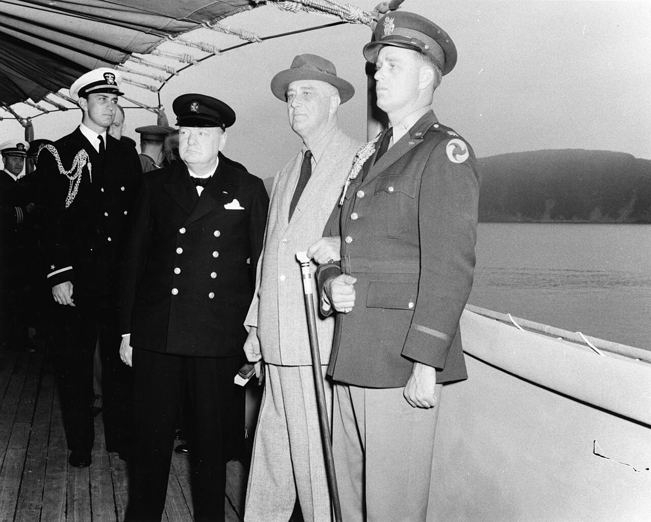 Winston Churchill and Franklin D. Roosevelt meet aboard USS Augusta; Elliott Roosevelt supports his father’s arm, with naval officers and officials nearby.