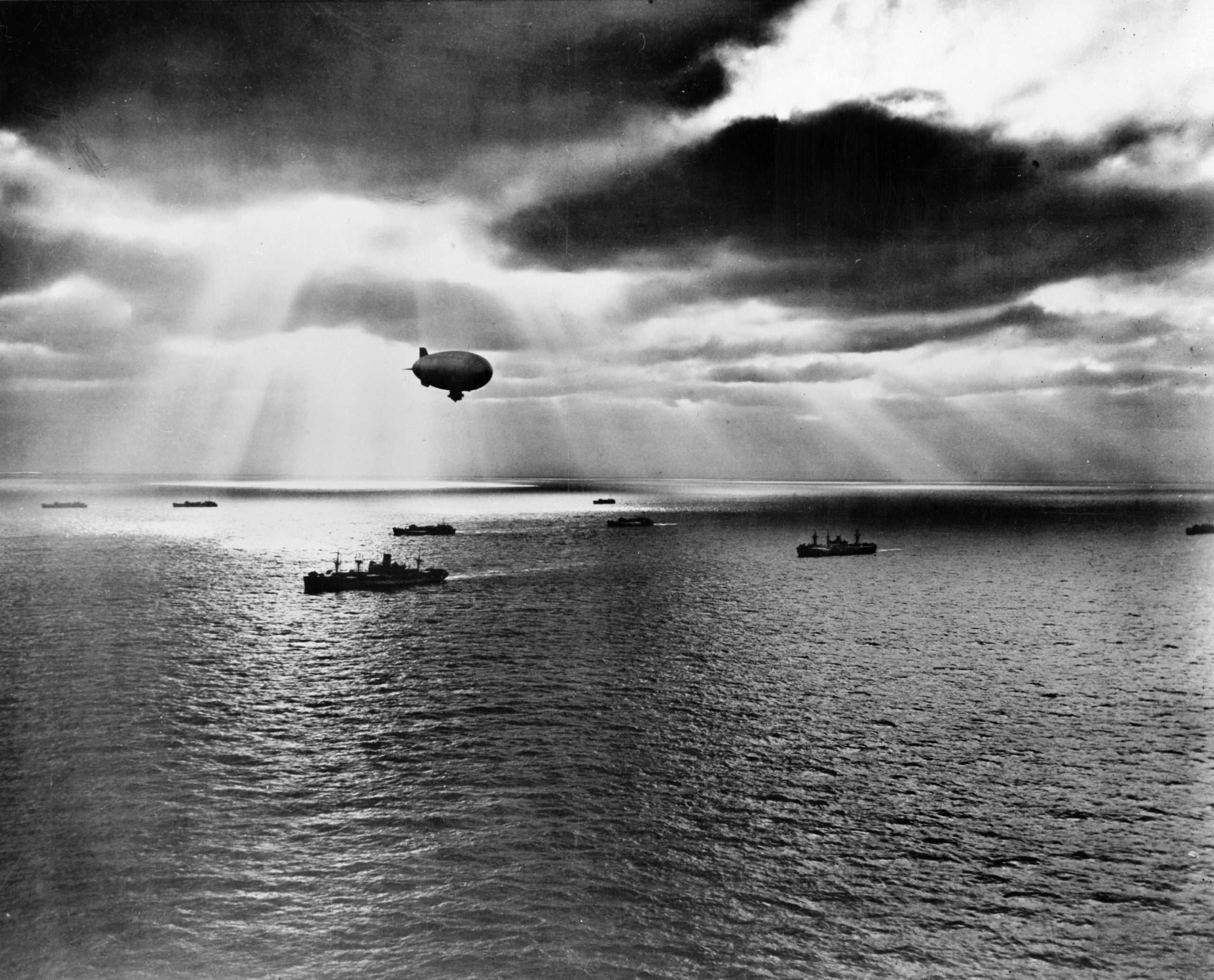 A U.S. Navy blimp patrols above merchant ships crossing the Atlantic at sunset in June 1943.