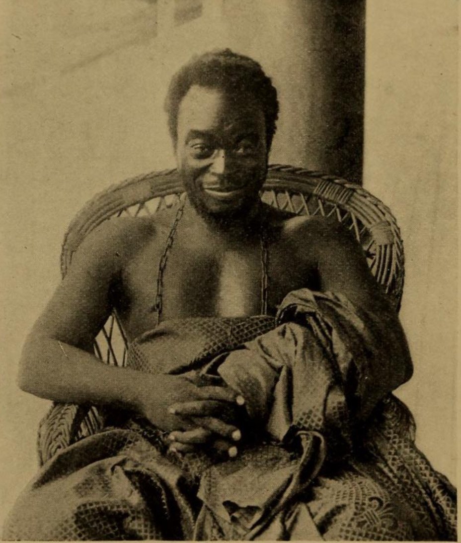 Oba Ovonramwen seated in a wicker chair aboard a vessel, with patterned cloth around his body