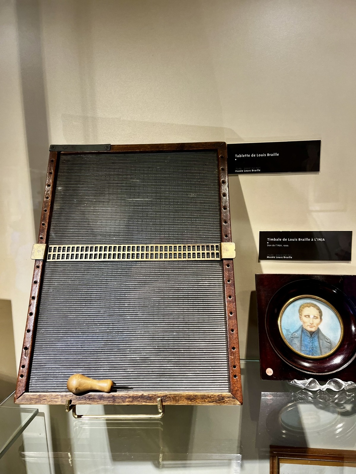 A historical braille writing slate displayed in a museum case