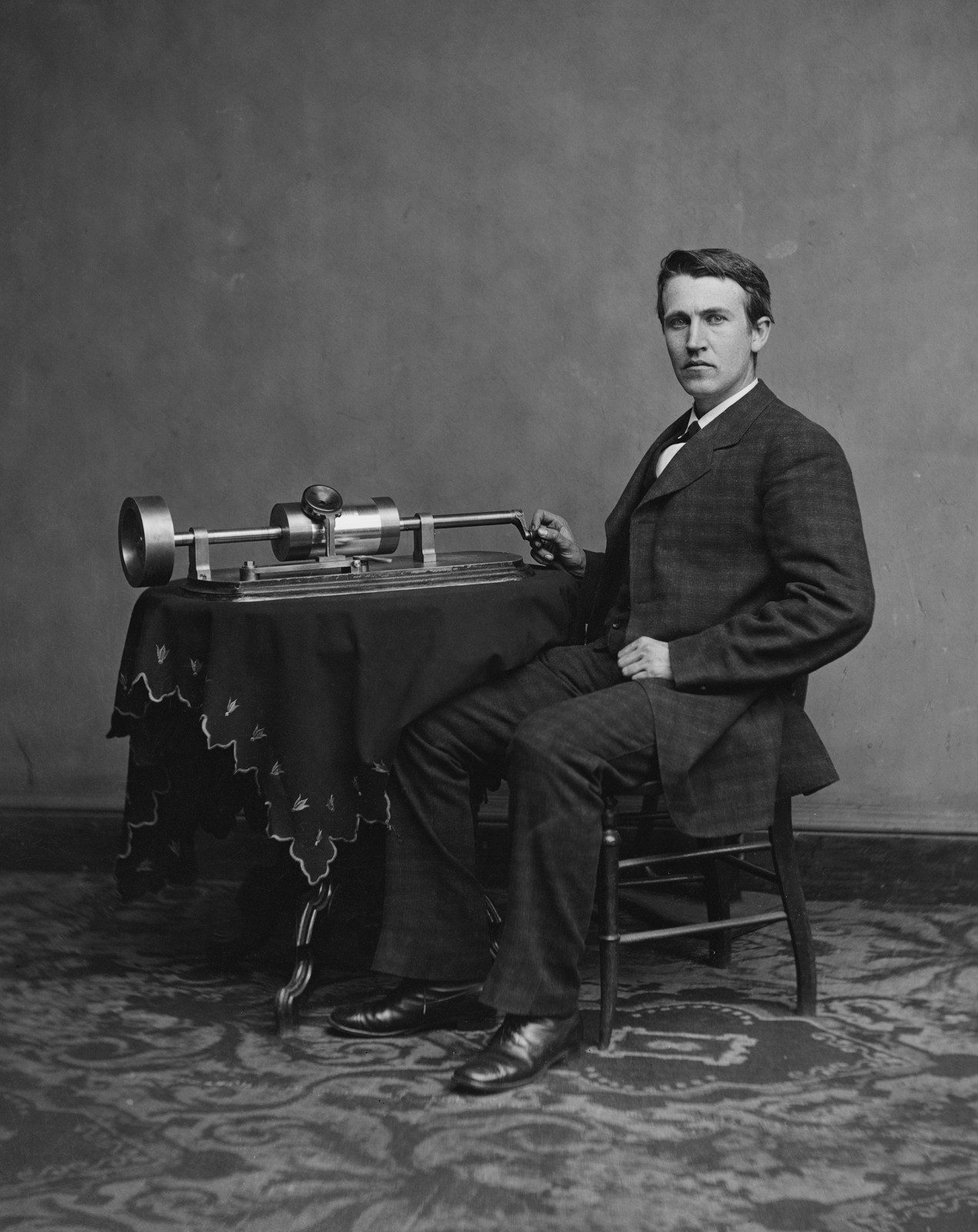 Thomas Edison seated beside an early phonograph in a studio portrait.
