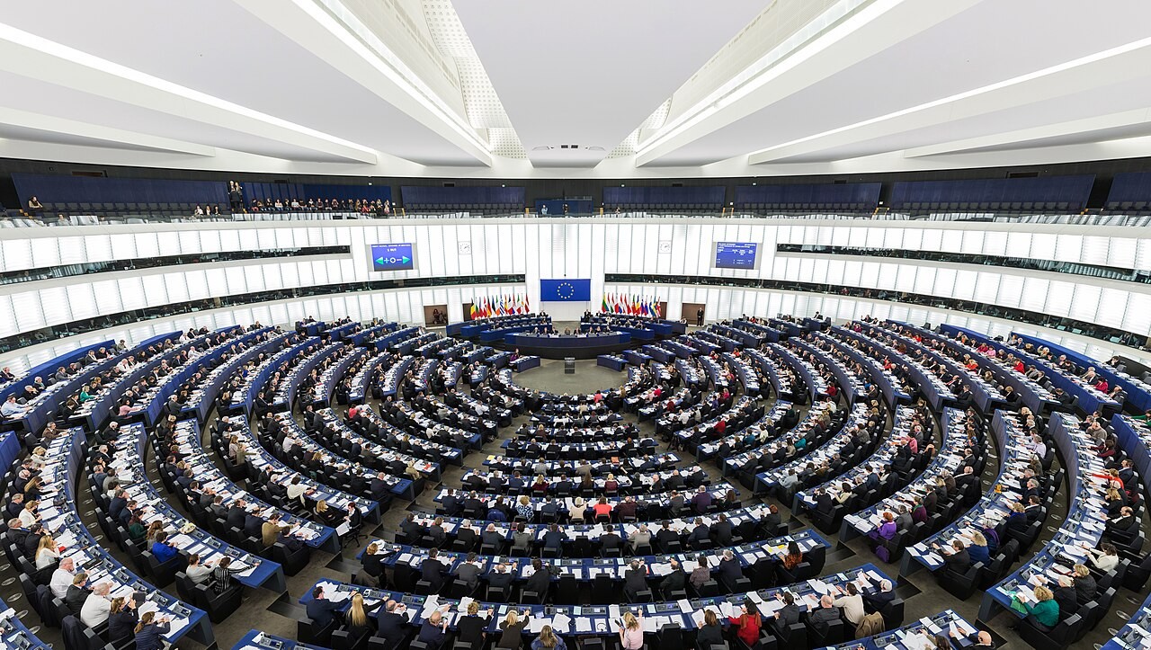 A wide view of the European Parliament’s Strasbourg hemicycle during a sitting, with members in semicircular rows.