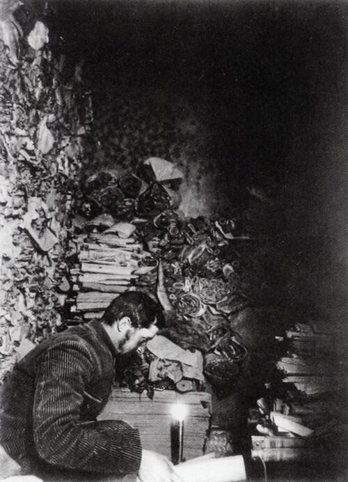 Paul Pelliot seated among dense stacks of manuscripts inside Cave 17