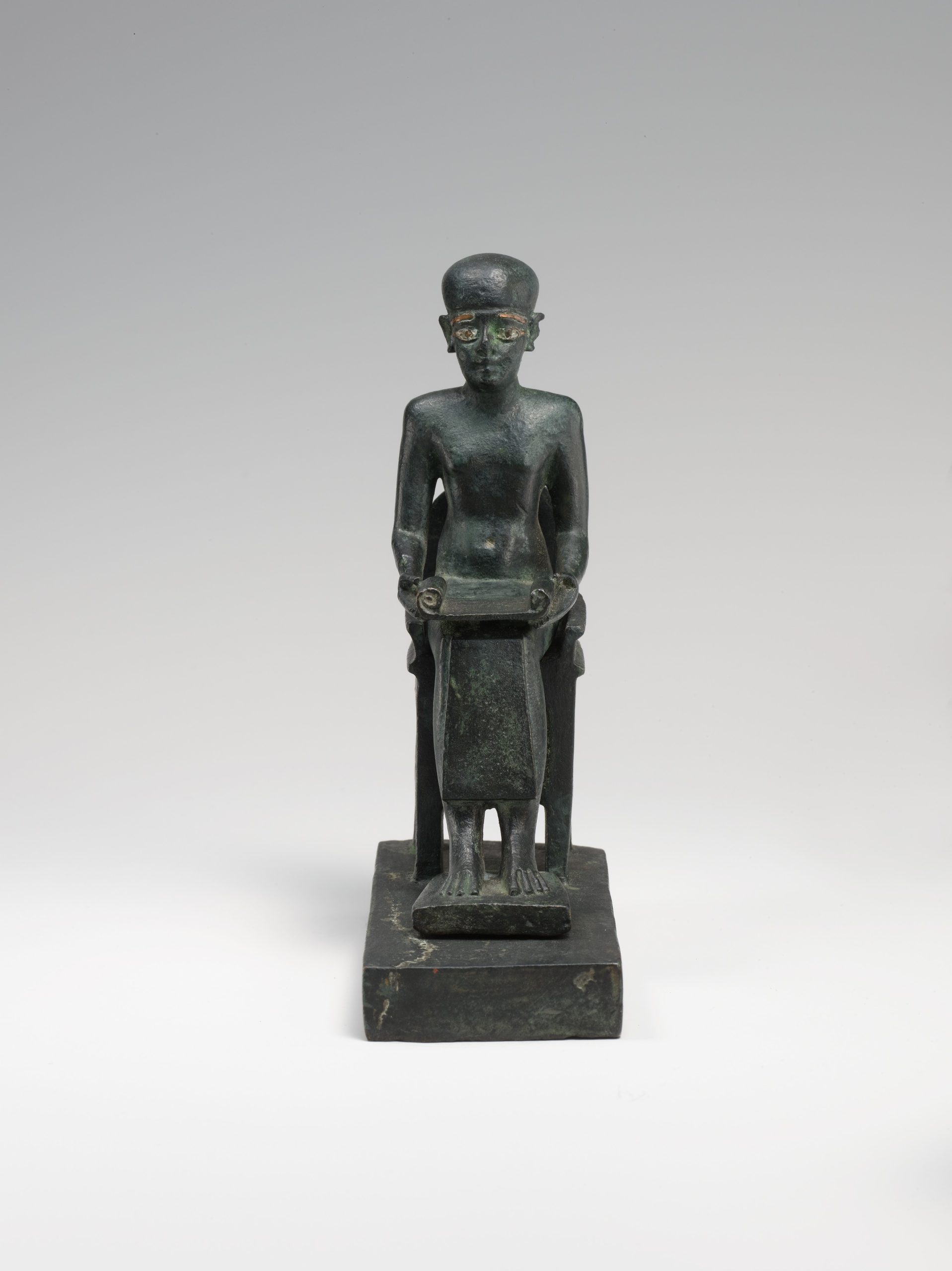 Small metal statue of Imhotep seated on an elaborate chair and holding an open scroll.