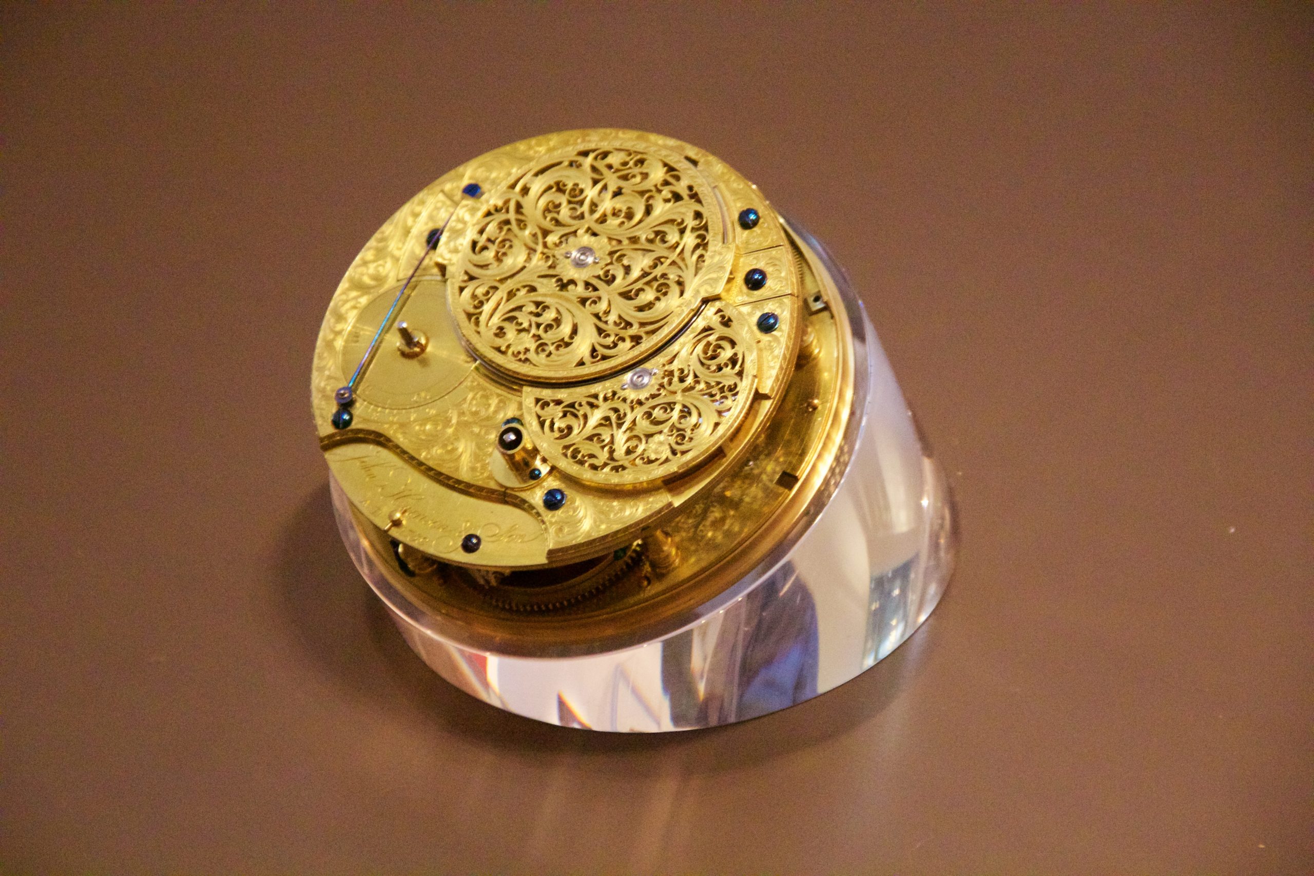 The gold-colored movement of Harrison’s H4 sea watch, with pierced metal covers, small blue screws, and exposed wheels.