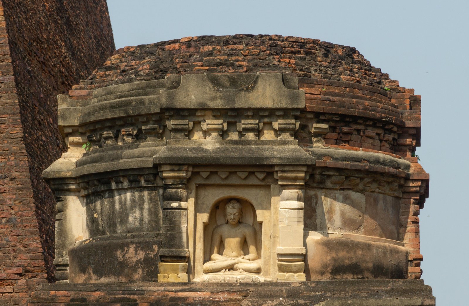 A seated Buddha in a stucco niche surrounded by molded decoration and weathered brickwork at Temple 3, Nalanda.