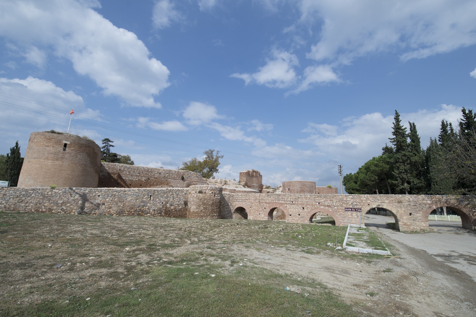 Stone and brick fortification walls and towers beside an arched water channel and grassy foreground at İznik.