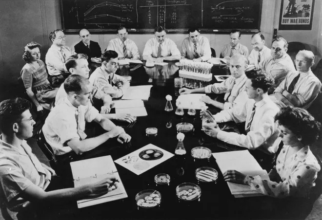 The USDA penicillin research team sits around a table with papers, laboratory glassware and culture dishes at Peoria in June 1944.