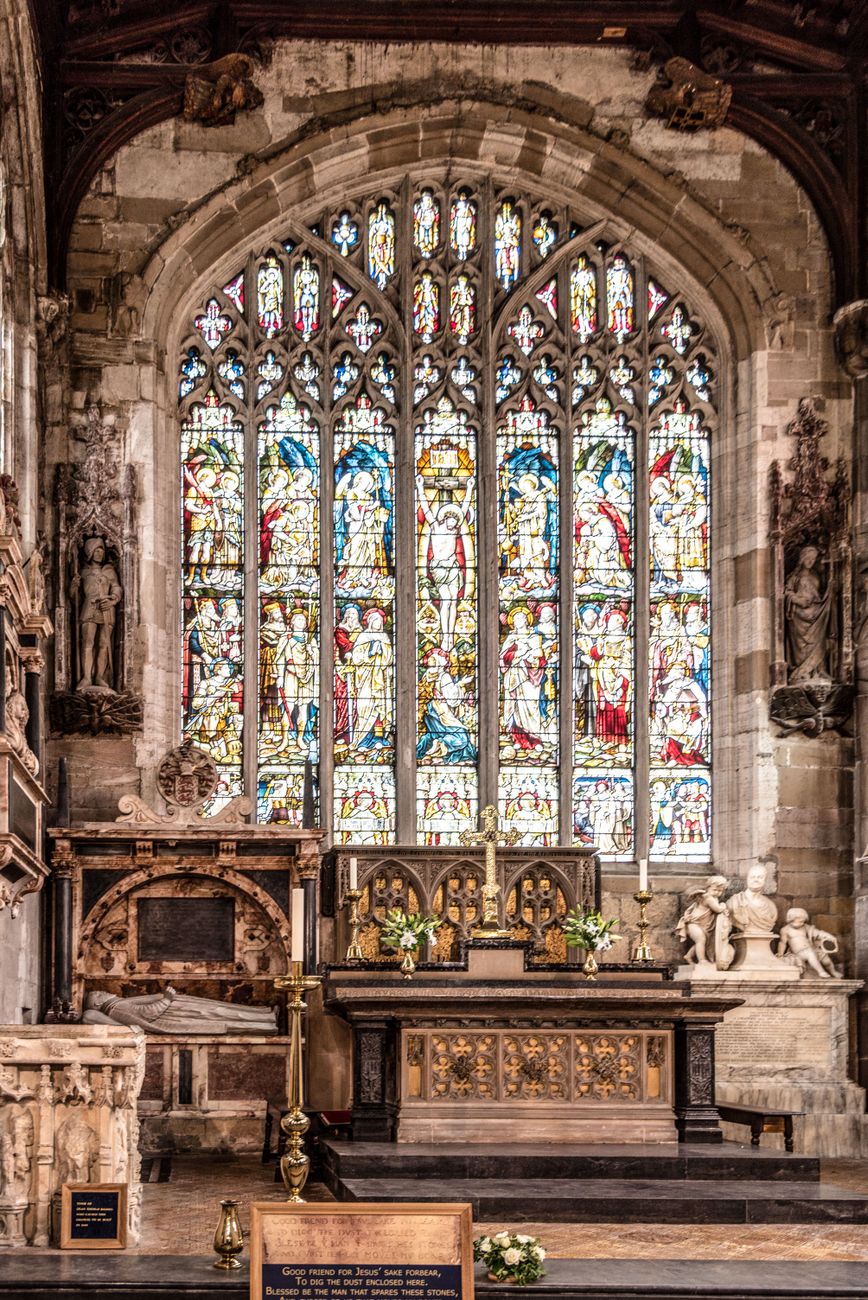 Church chancel with stained-glass windows, an altar, memorials and a grave marker in the foreground.