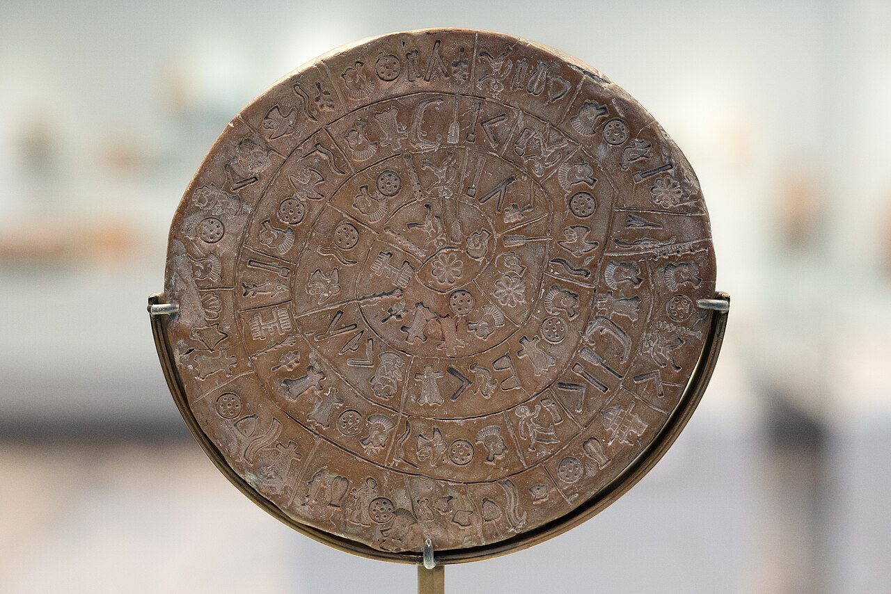 Side A of a brown clay disc held in a museum mount, with stamped figures arranged in a divided spiral and a rosette-like form near the centre.