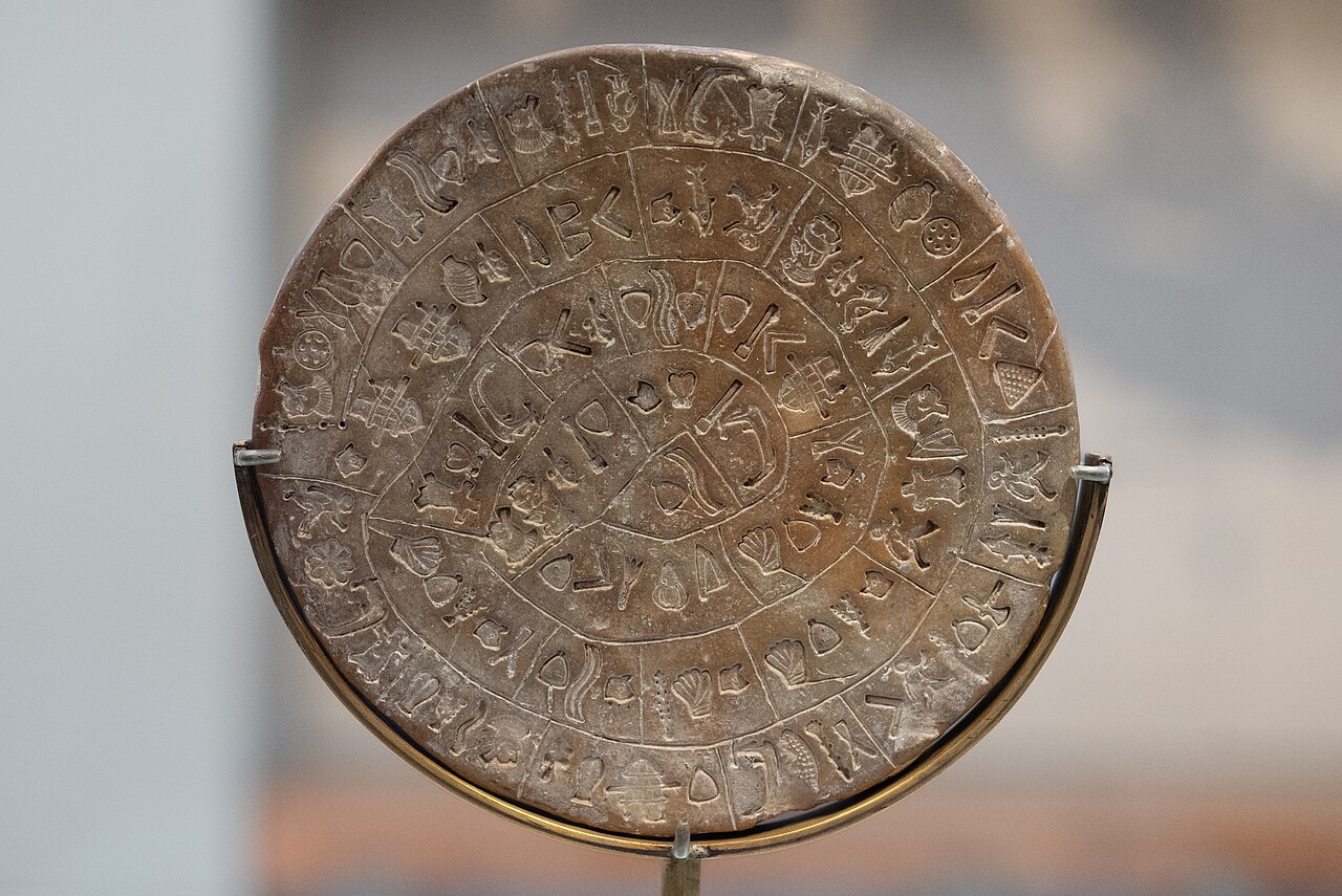 Side B of the clay Phaistos Disc, with spiralling rows of stamped forms including animal-like shapes, vessels and repeated angular marks.