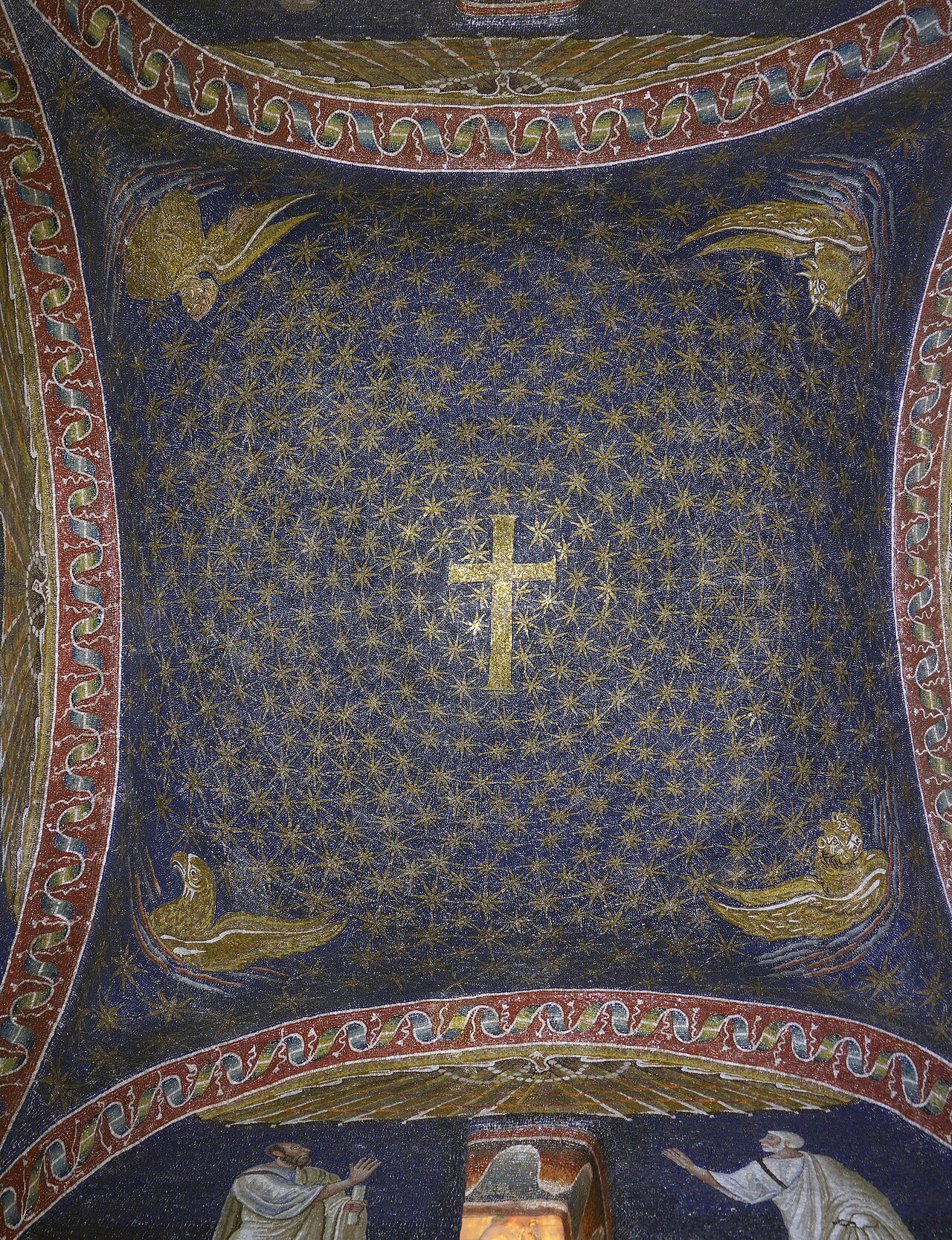 Blue mosaic vault filled with golden stars around a central cross, bordered by red and white bands and four winged creatures.