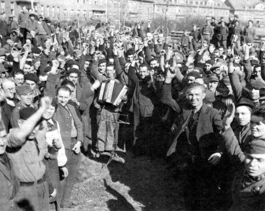 A crowd of displaced people waves beside an accordion player at the former Kemmel Barracks in Trier in 1945.