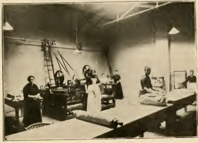 Historical photograph of women and other figures beside mangling machines and large tables in the Hornsey Road laundry.