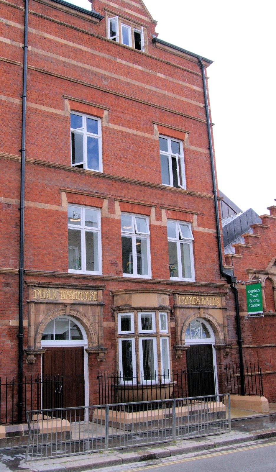 Red-brick Kentish Town building with arched ground-floor entrances and carved lettering for the public washhouse and ladies baths.