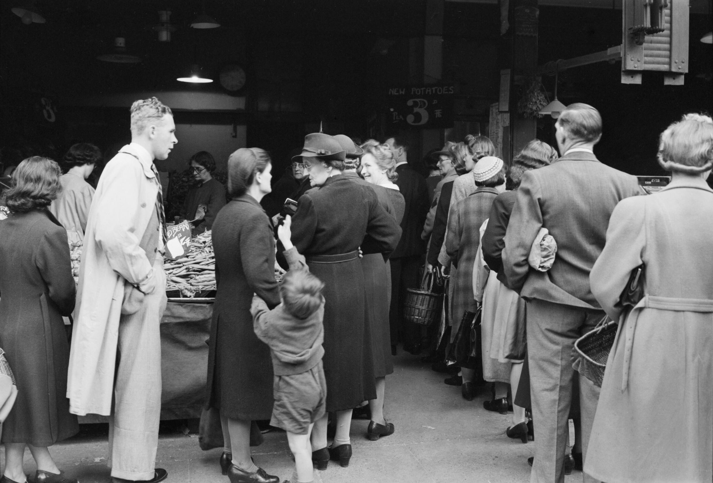 People carrying shopping bags and baskets queue outside a greengrocer in Wood Green, London, in 1945.