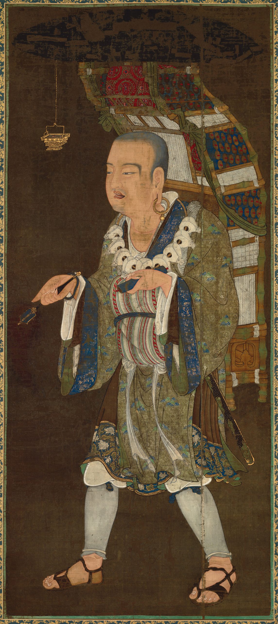 Fourteenth-century Japanese painting of Xuanzang in a patterned robe, carrying a tall bundle of Buddhist scriptures on his back.